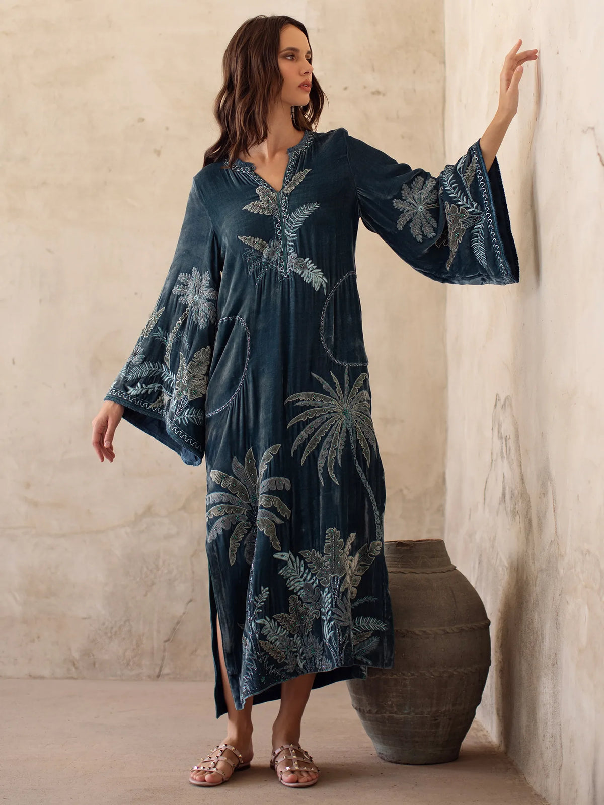 Woman wearing a dark blue dress with floral patterns against a neutral wall.