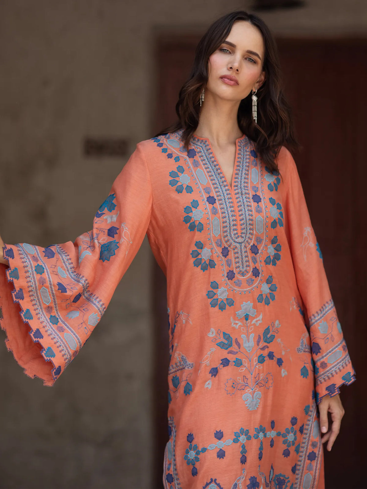 Woman wearing a peach-colored embroidered dress with bell sleeves against a neutral background