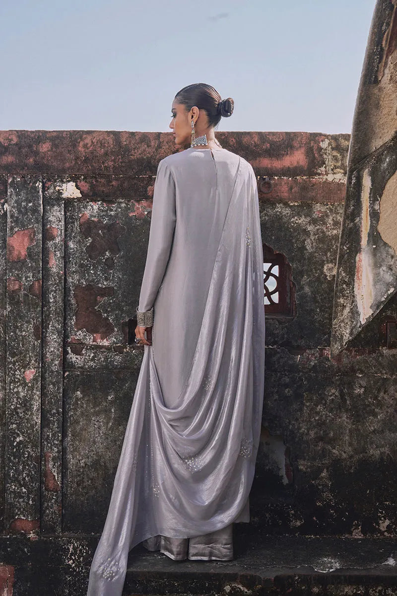 Woman in a gray saree standing in front of a textured wall.