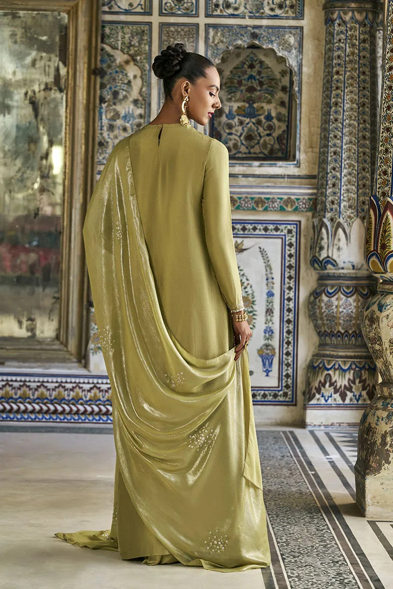 Woman in a green saree standing in an ornate room with decorative tiles.