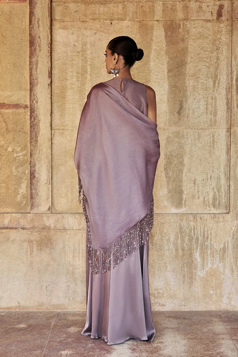 Woman wearing a lavender saree with a textured wall background