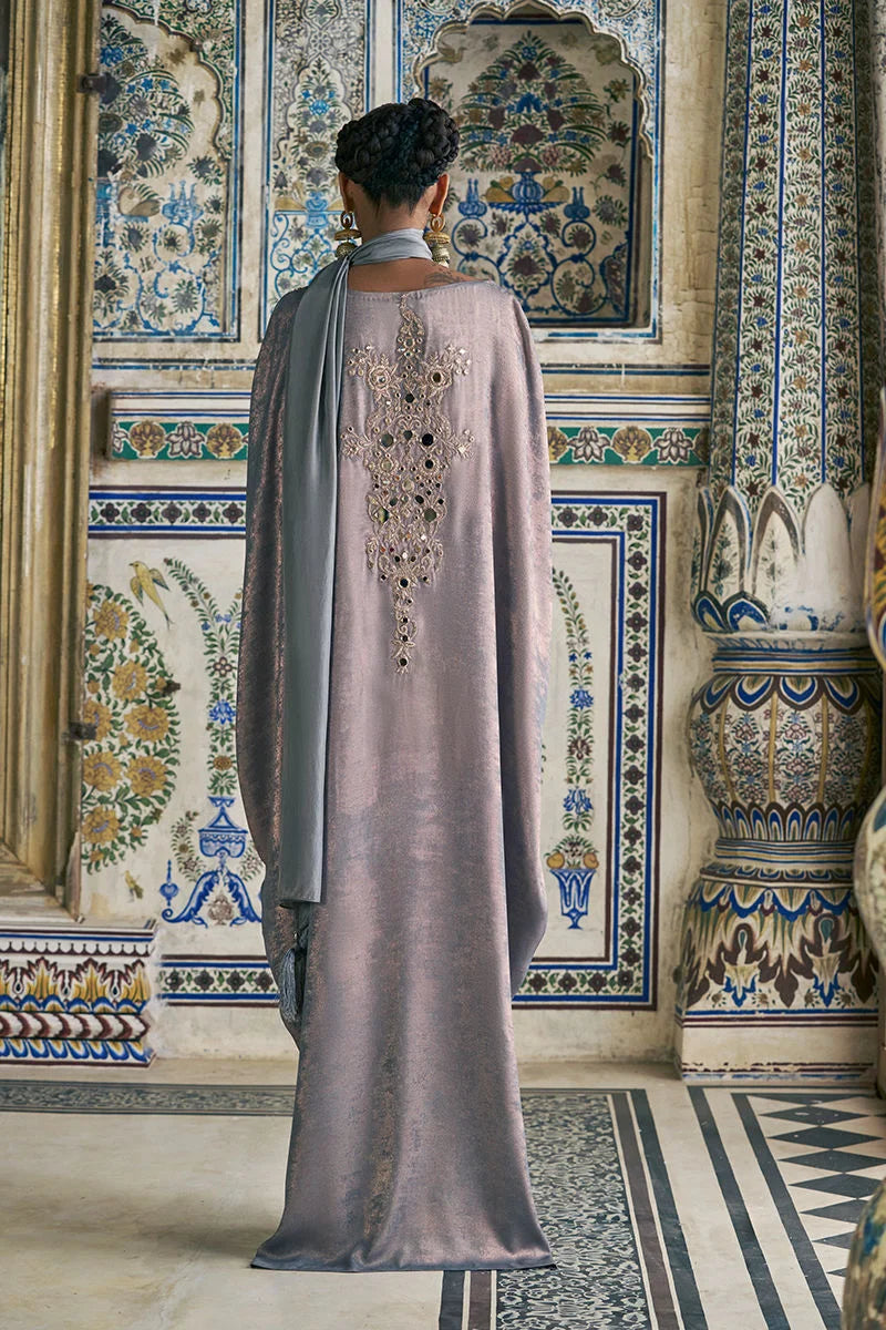 Person wearing a long, embroidered garment in a decorative interior setting.