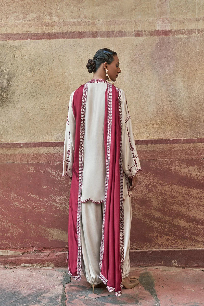 Woman wearing a traditional outfit with pink and white patterns against a textured wall.