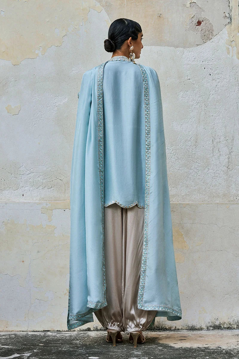 Woman wearing a light blue embroidered dupatta over a beige outfit against a textured wall.