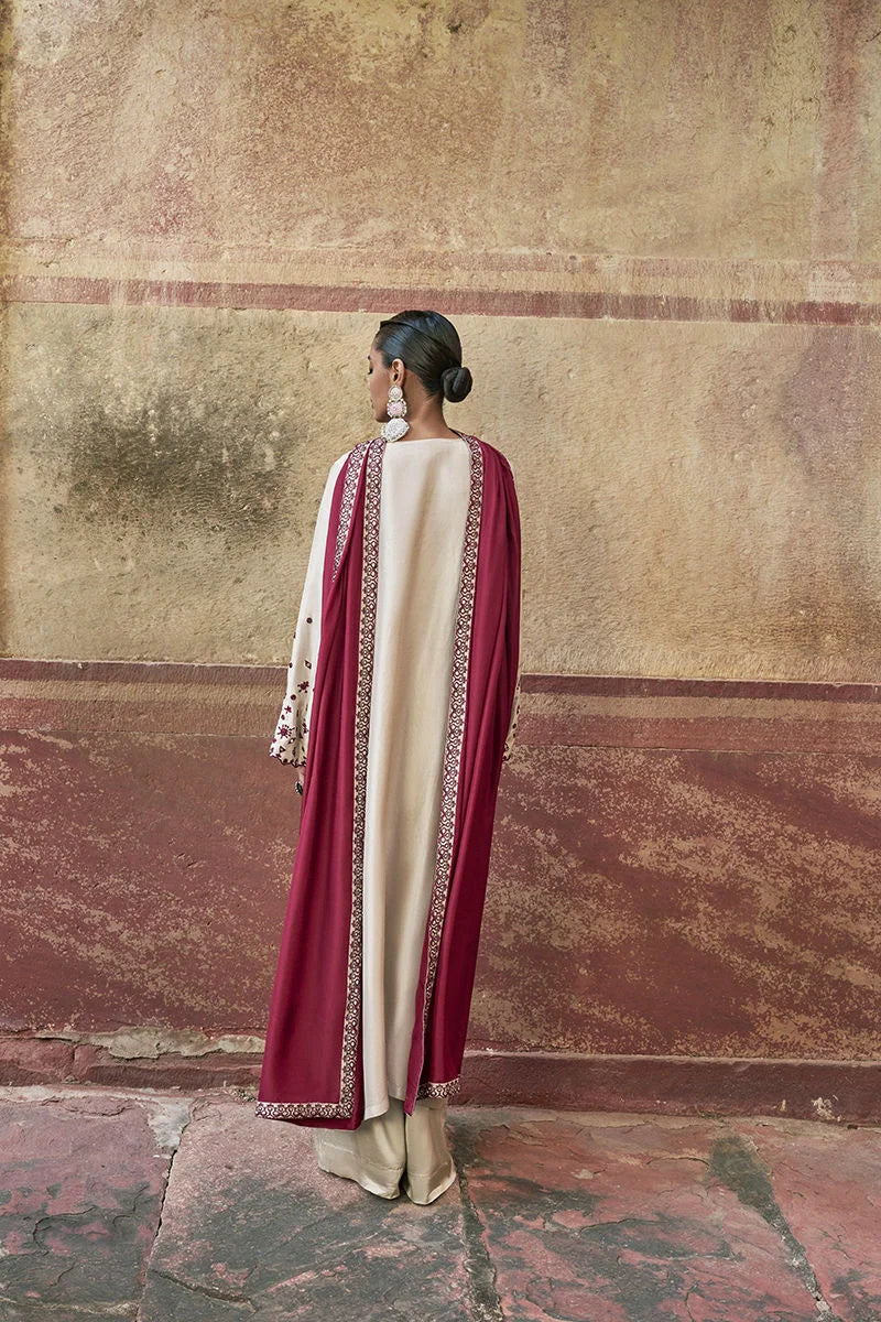 Woman wearing a traditional outfit with maroon and cream colors against an old wall.