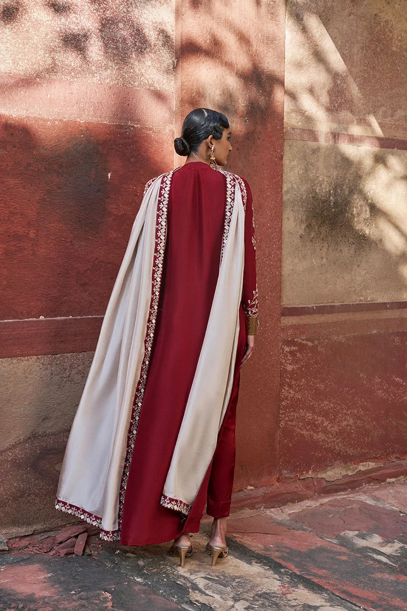 Woman in a red and white traditional outfit standing against a textured wall.