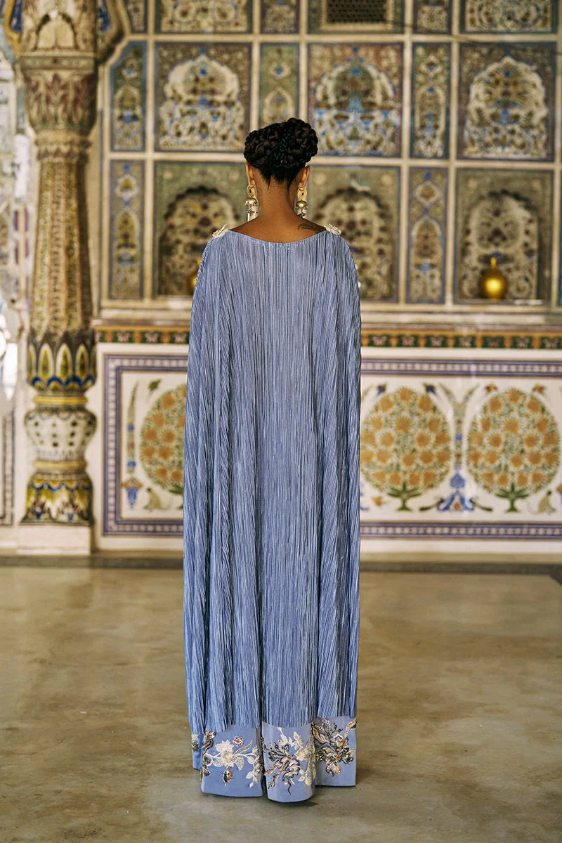 Woman wearing a long, light blue dress with floral patterns in a decorative interior setting.