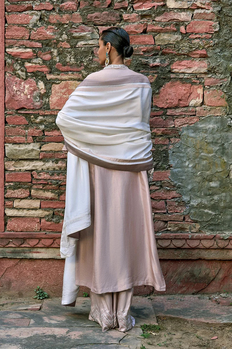 Woman wrapped in a white shawl against a stone wall