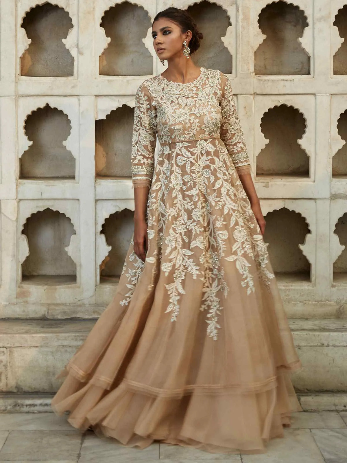 Woman wearing a beige lace dress in front of an architectural wall.