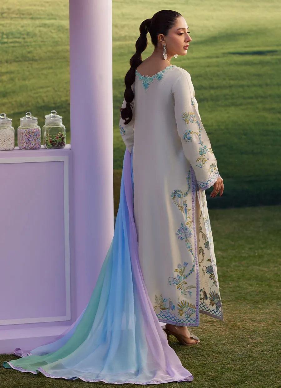 Woman in a long, light-colored dress with floral patterns standing in a grassy area.