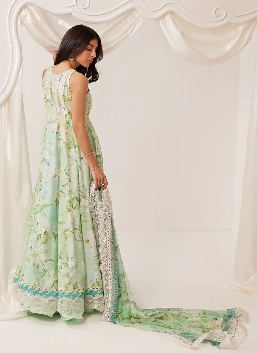 Woman wearing a light green floral dress with a matching shawl against a white curtain background