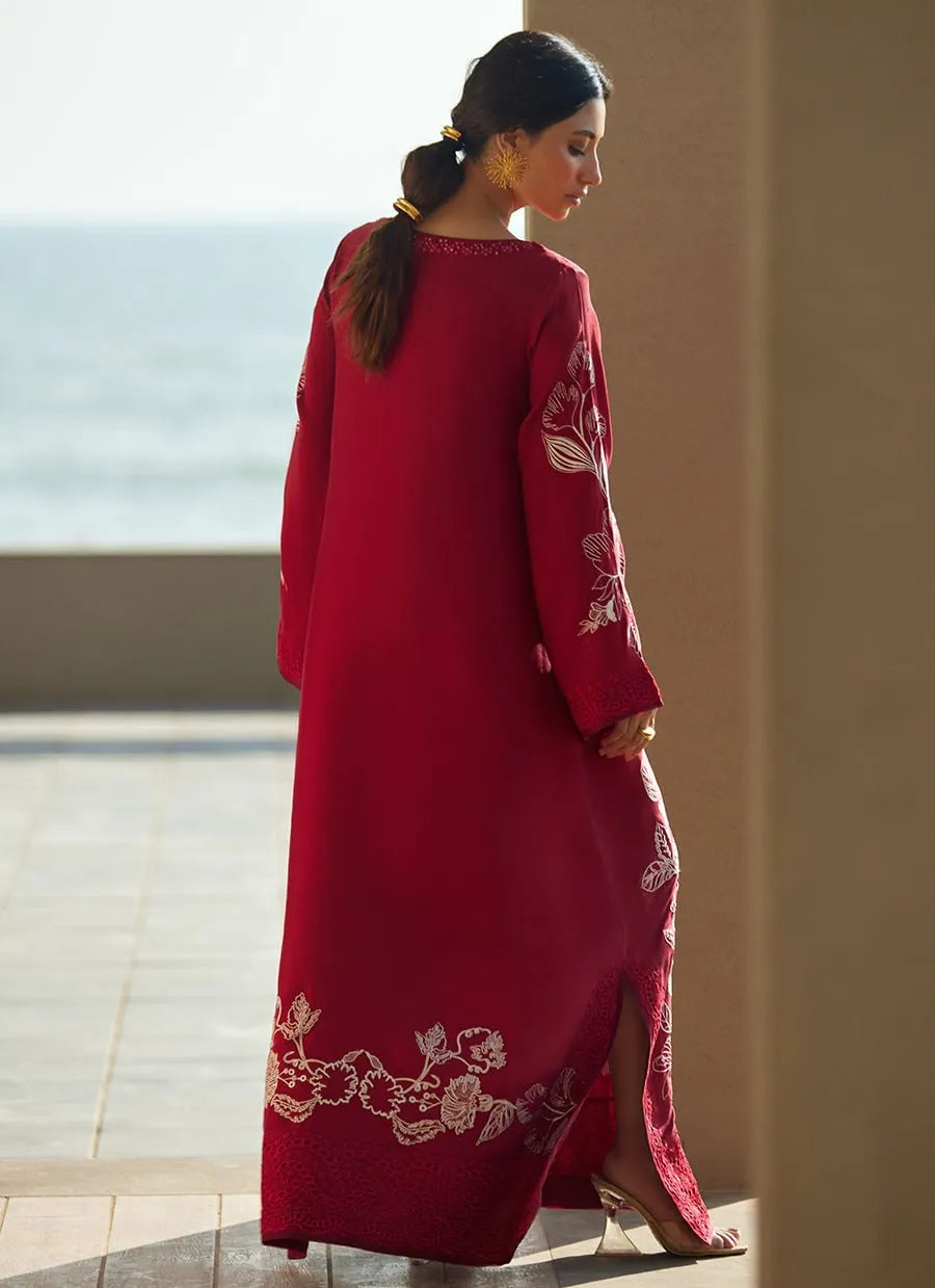 Woman wearing a red dress with white embroidery by a window with a view of water.