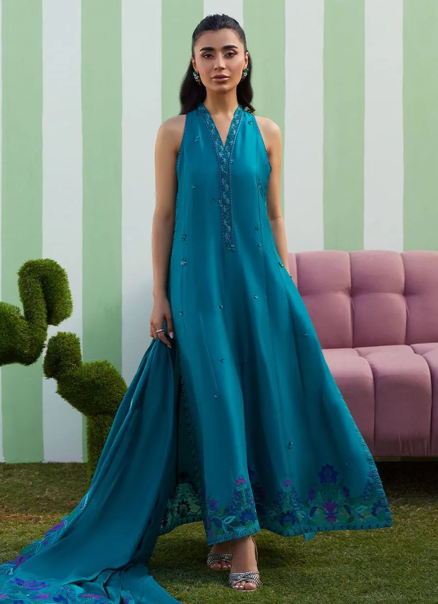 Woman in a teal dress standing in front of a striped wall with a pink couch and green plant.