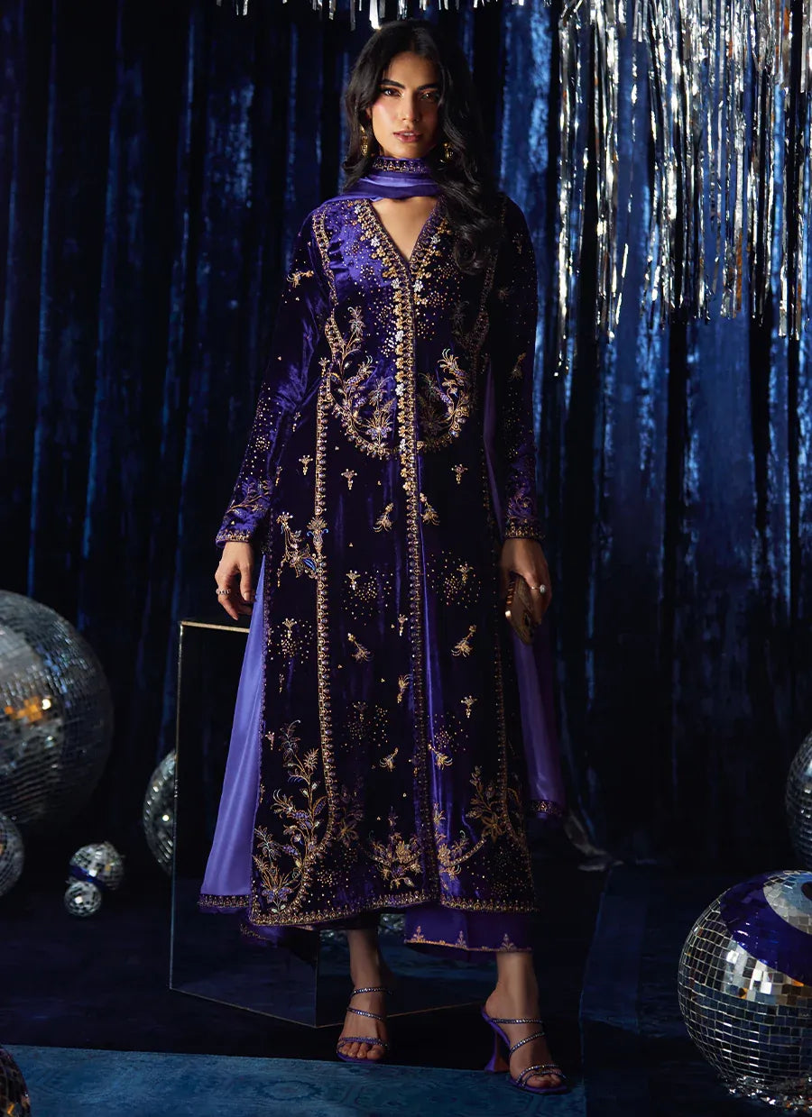 Woman in a purple embroidered dress standing against a dark blue curtain with disco balls.