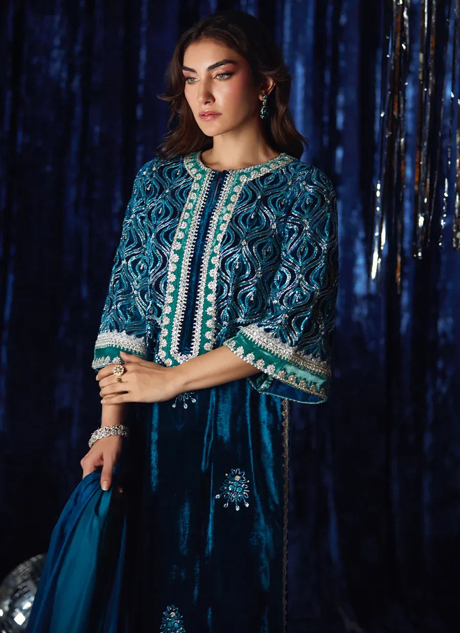 Woman wearing a blue embroidered outfit against a dark blue curtain.