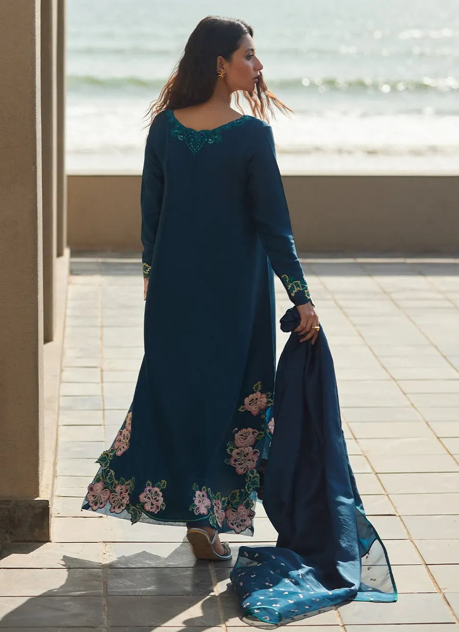 Woman in a long, dark blue dress with floral patterns standing on a tiled floor.