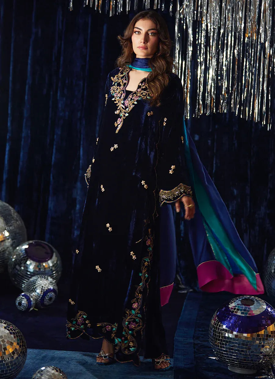 Woman in a dark blue embroidered outfit with colorful accents against a festive background.