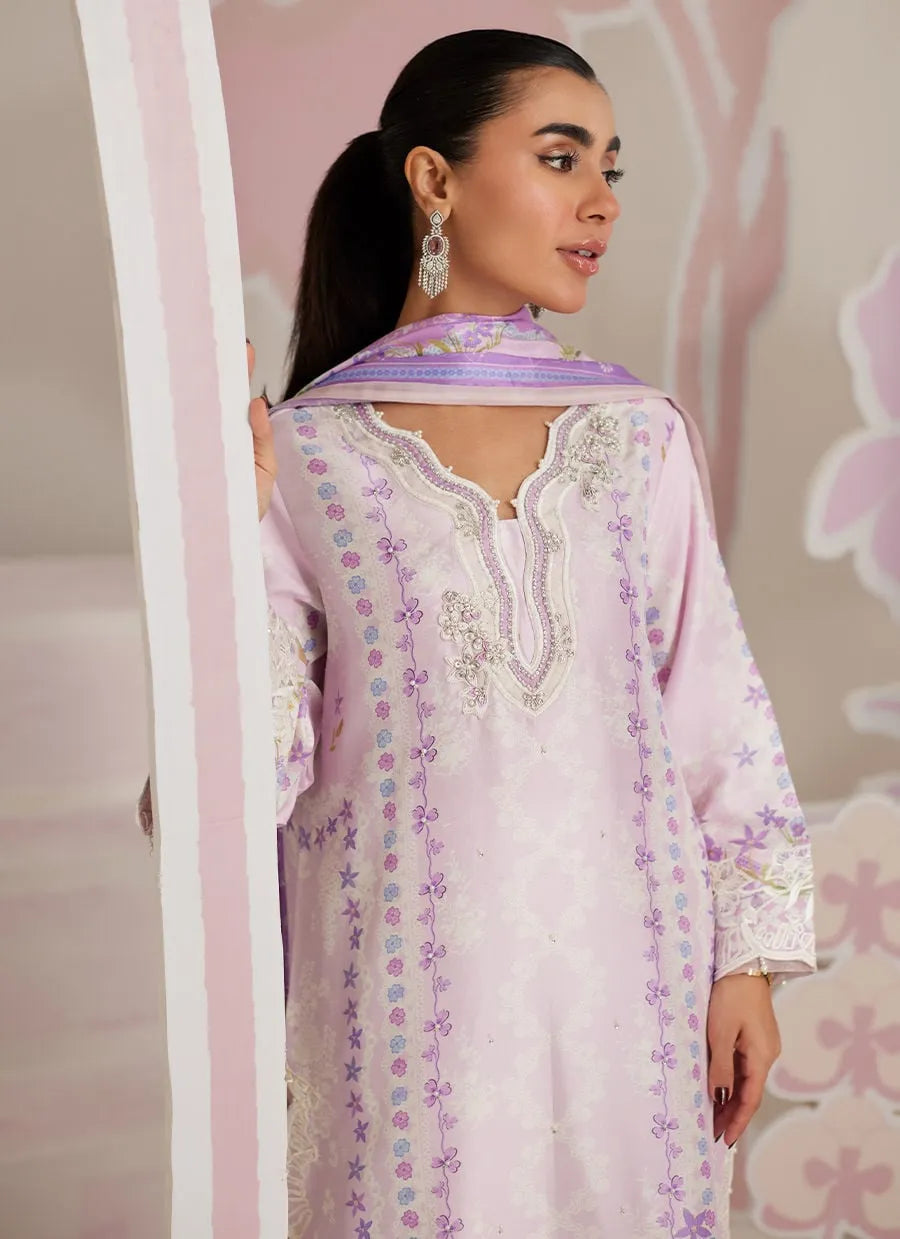 Woman wearing a light purple embroidered dress with a matching dupatta in front of a decorative pink background.