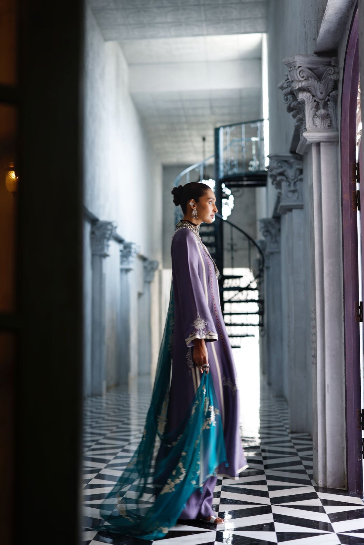 Woman in a purple and blue outfit standing in a grand hallway with black and white checkered floor.