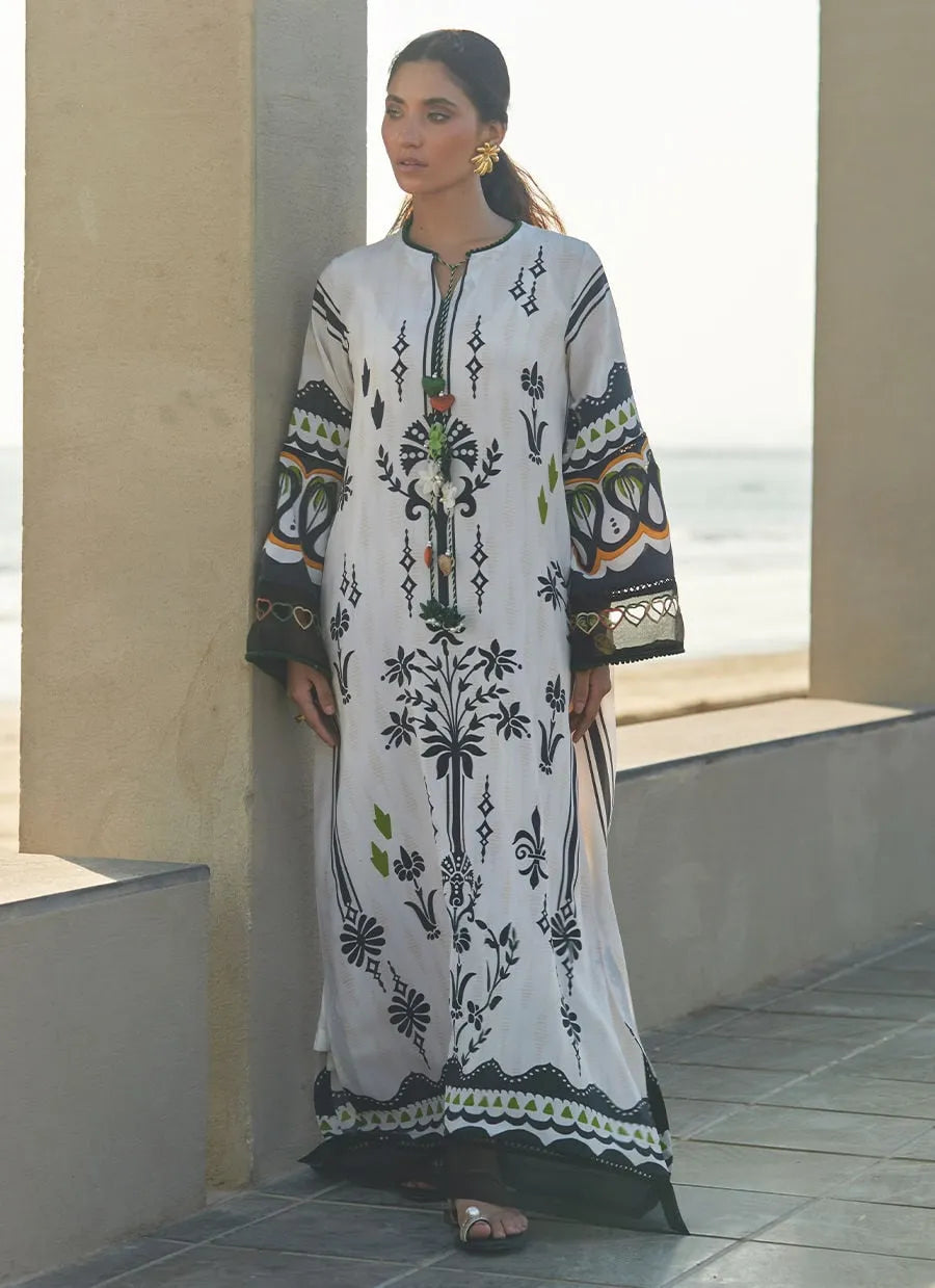 Woman wearing a long, embroidered dress standing on a sunlit walkway.