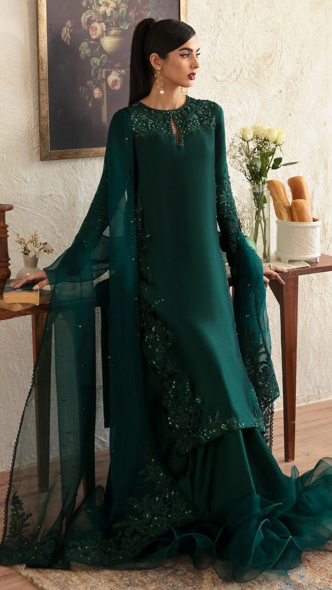 Woman in a green traditional outfit with floral patterns in an indoor setting.