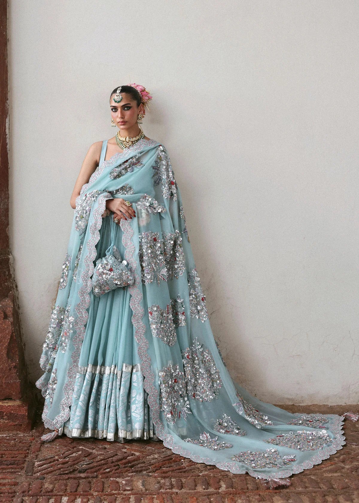 Woman in a light blue saree with silver embroidery against a plain wall.