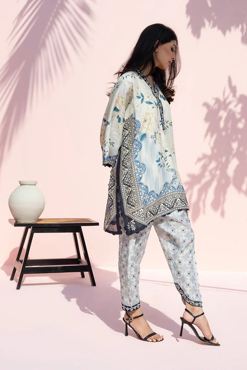 Woman wearing a floral outfit with a pink background and a small table.
