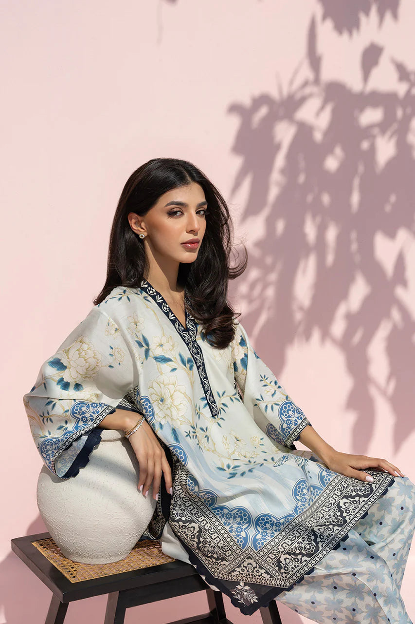 Woman in a floral outfit sitting on a stool against a pink wall with shadow patterns.