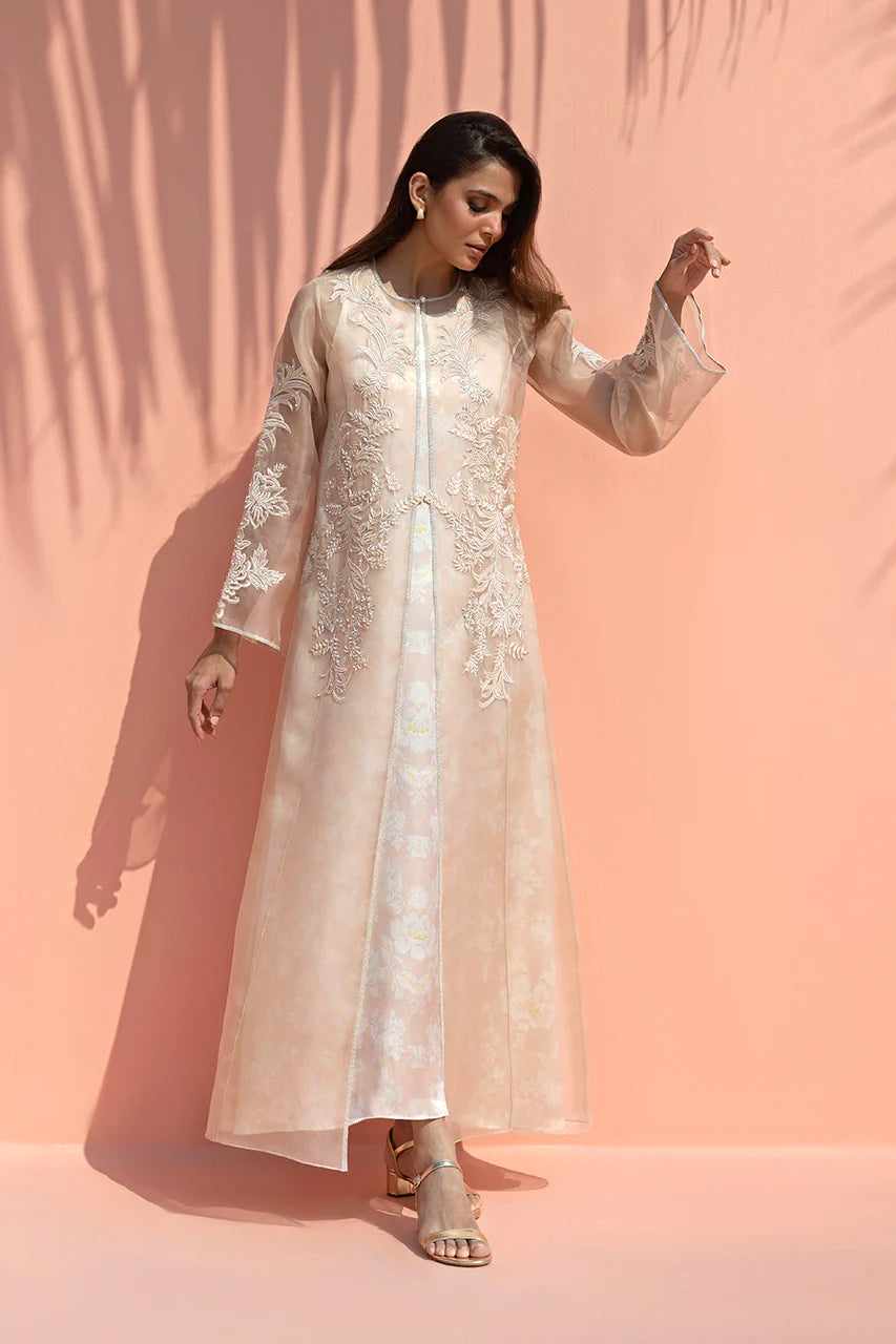 Woman wearing a long, light-colored embroidered dress against a pink background