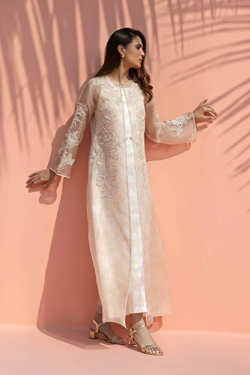 Woman wearing a light pink embroidered outfit against a peach background