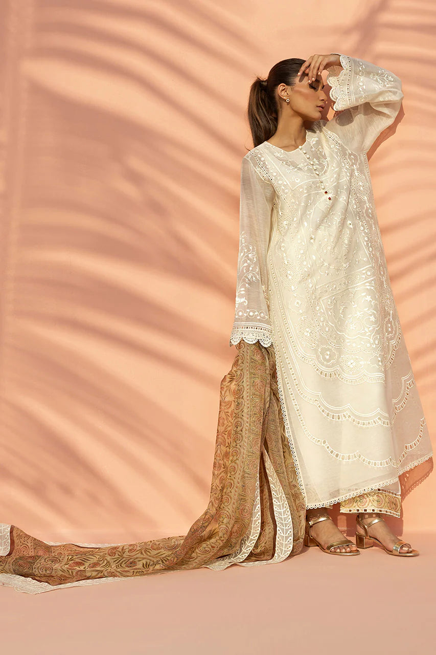Woman in a traditional outfit with a long, flowing design against a pink background