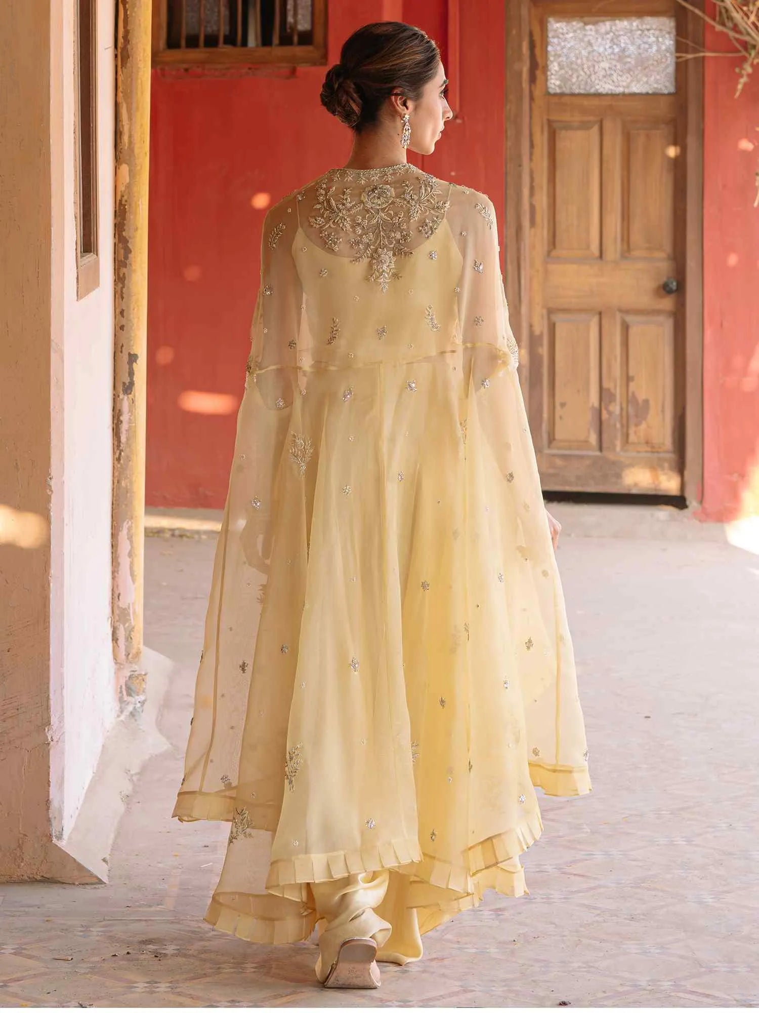 Woman in a light yellow embroidered traditional outfit standing in front of a red wall.