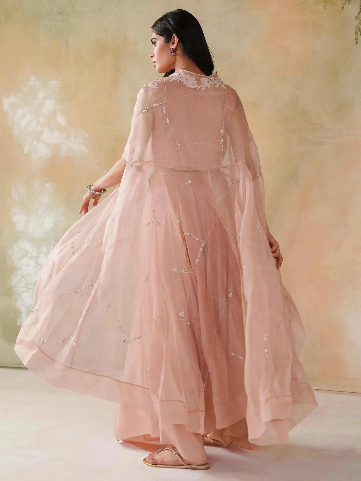 Woman wearing a light pink embroidered outfit against a soft, blurred background