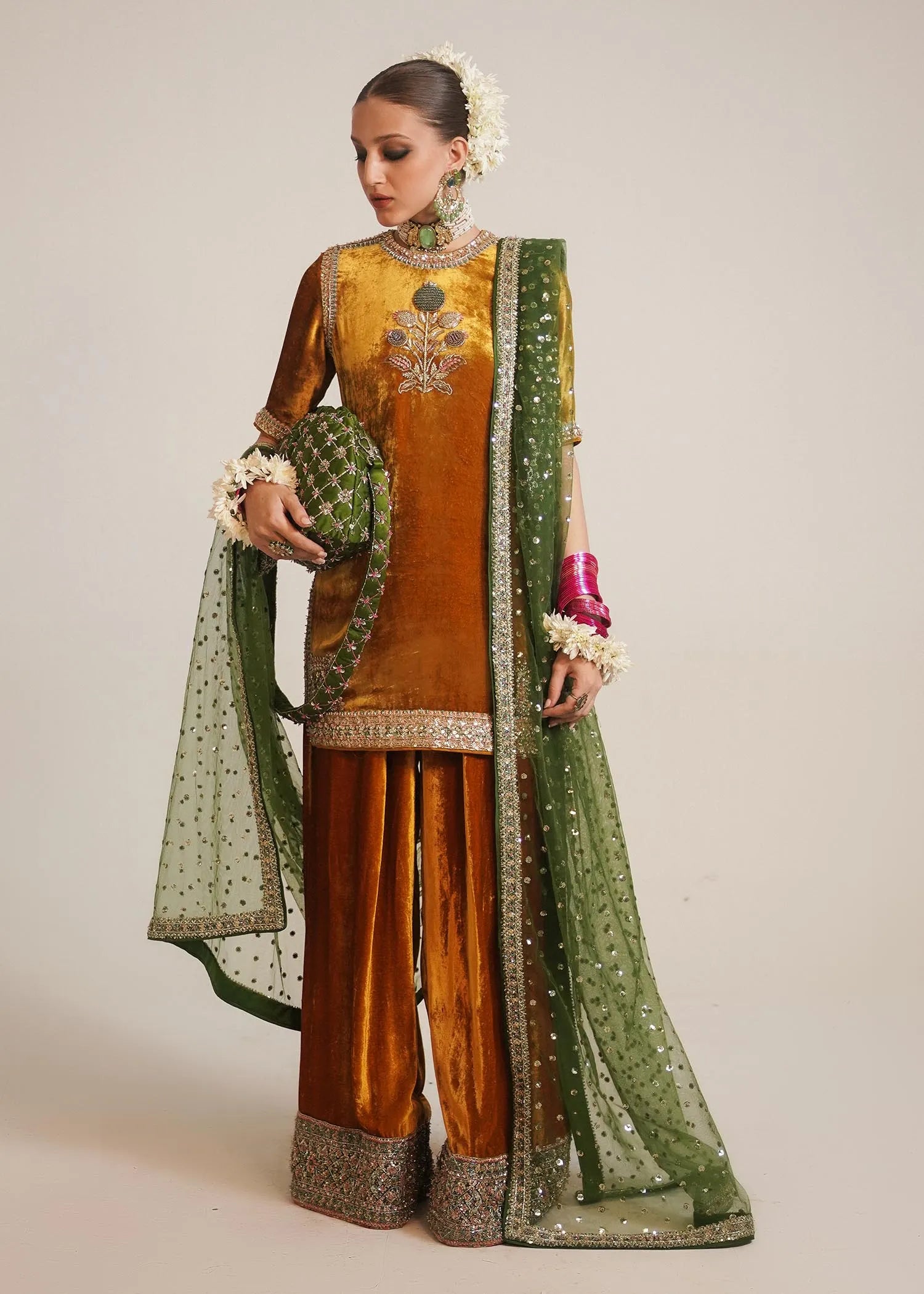 Woman wearing a traditional outfit with a green dupatta and orange top on a plain background