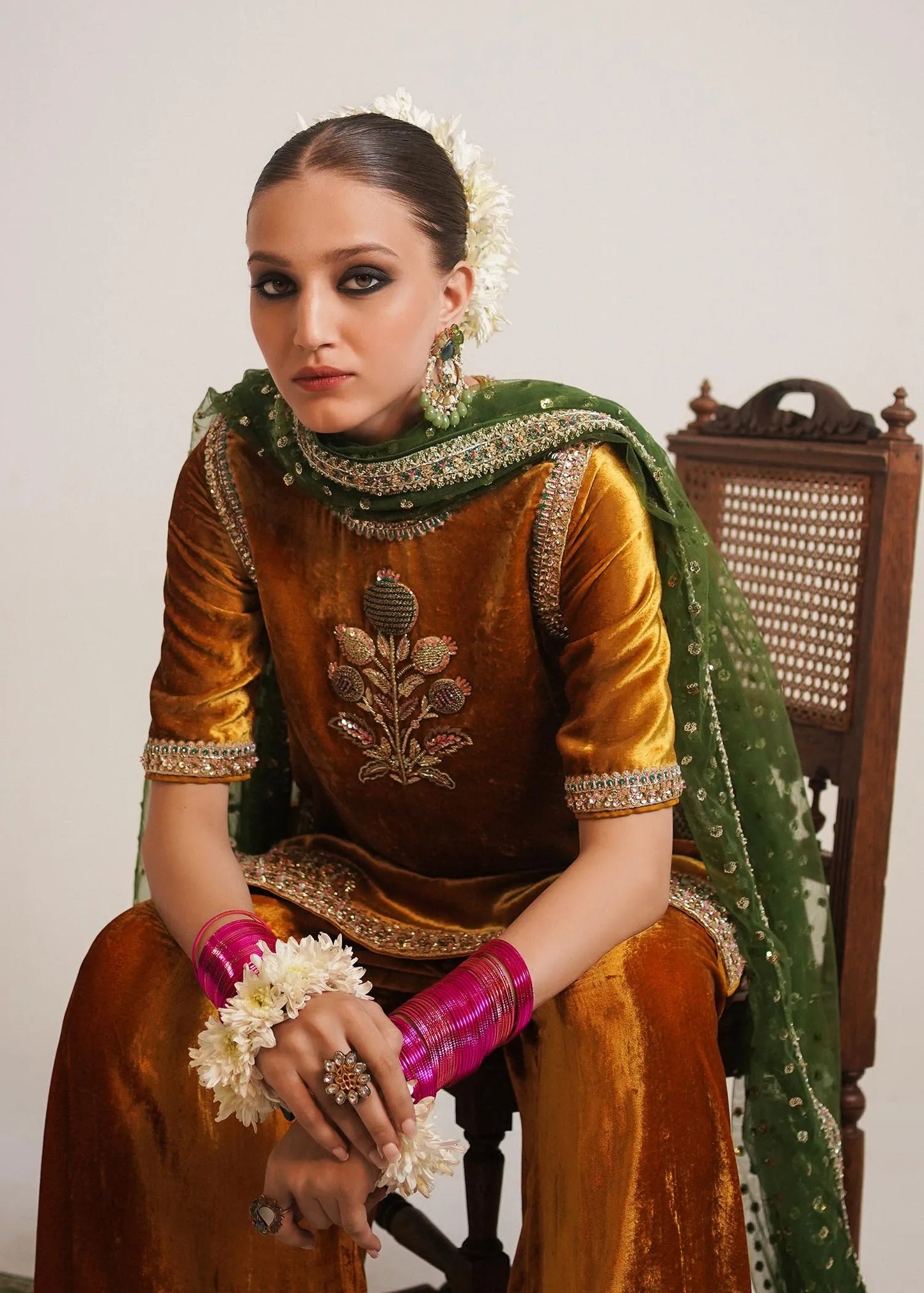 Woman in traditional attire with green dupatta and gold blouse sitting on a chair.