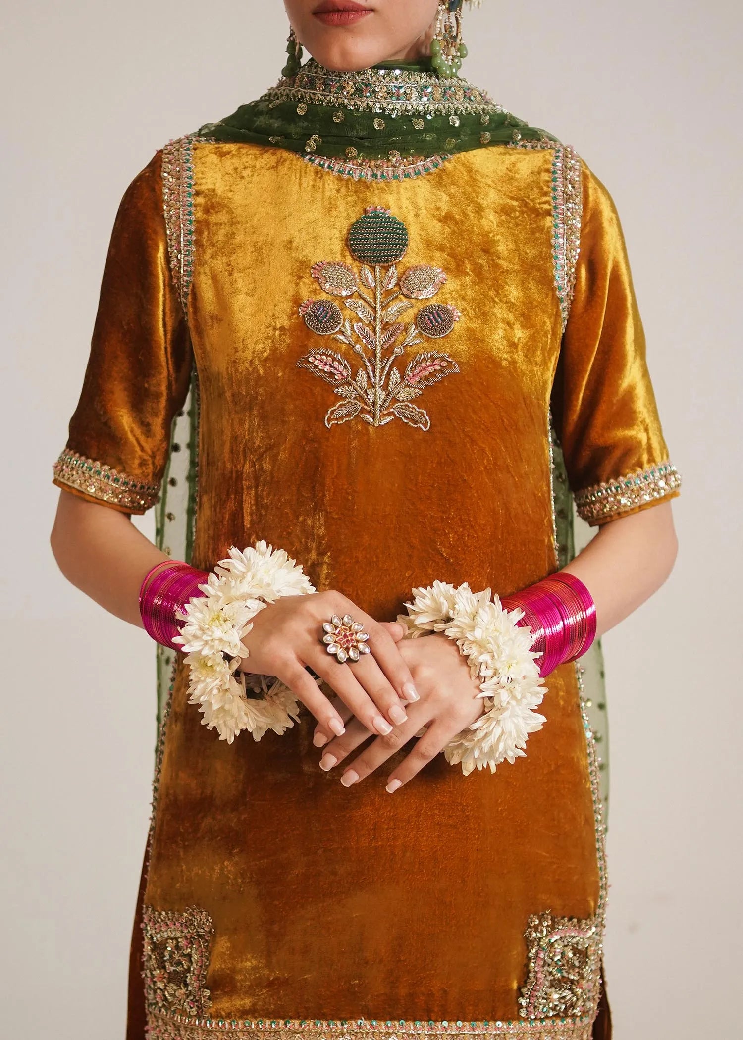 Traditional outfit with gold and green details, held by a person with floral decorations.