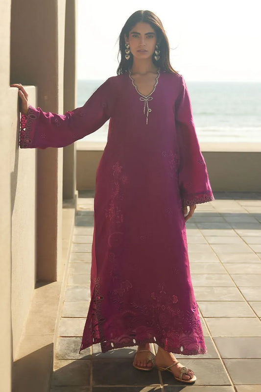 Woman in a long, embroidered pink dress standing on a rooftop with ocean view.
