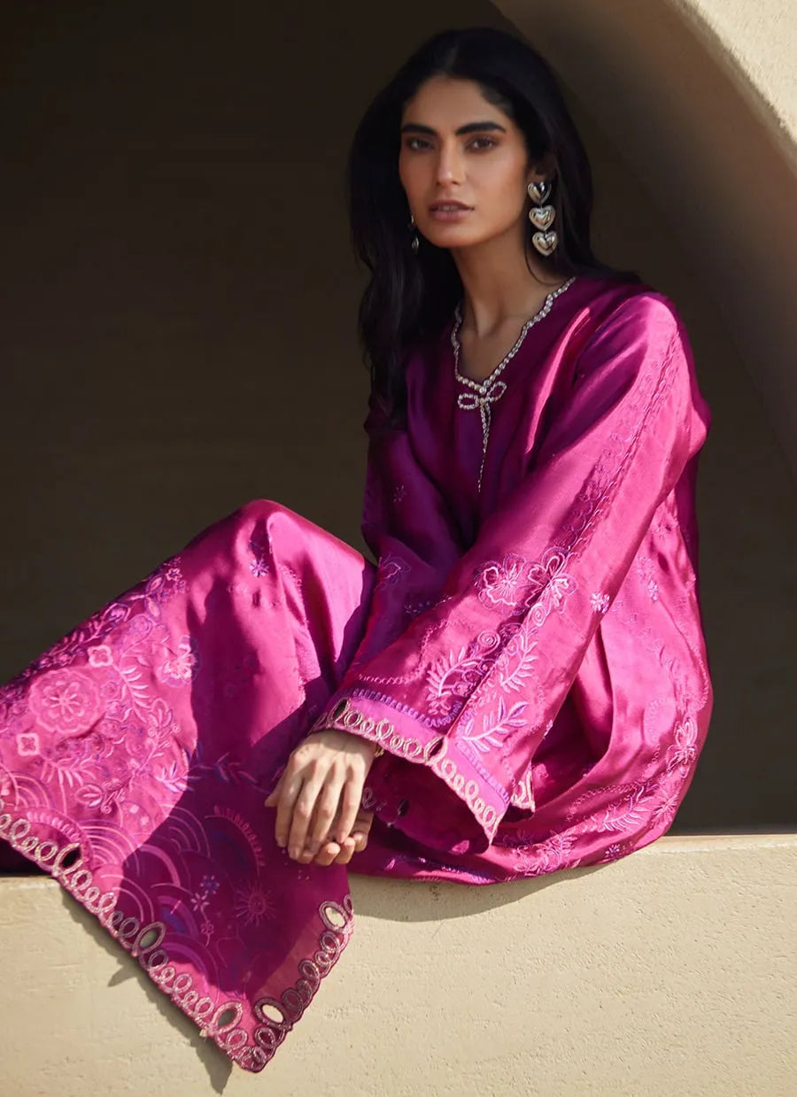 Woman wearing a pink traditional outfit with intricate patterns, sitting against a neutral background.