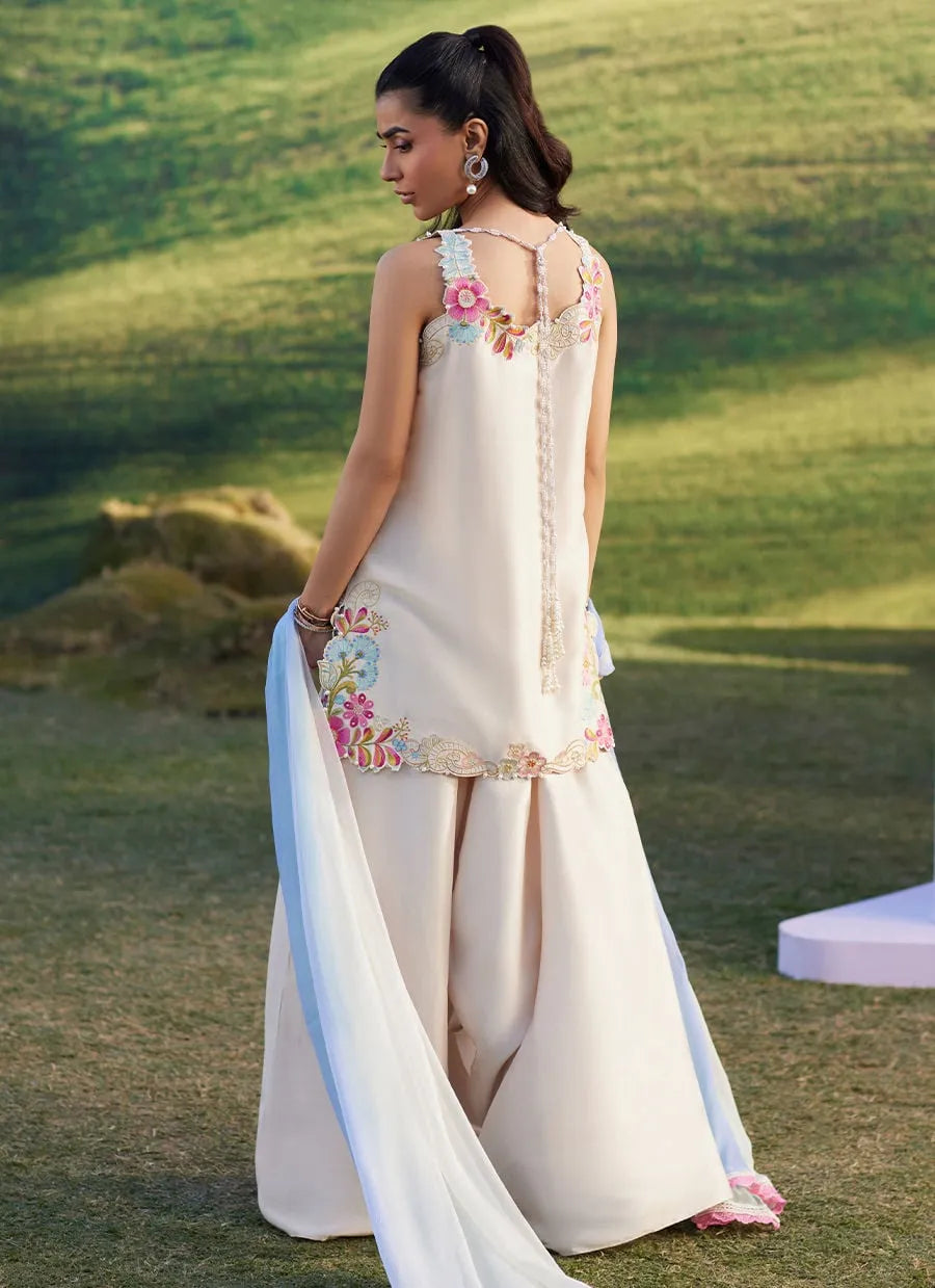 Woman in a white saree with floral embroidery standing on grass