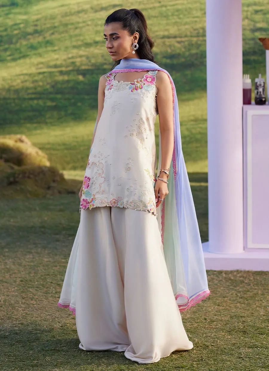 Woman in a traditional outfit with floral top and light pants standing outdoors.