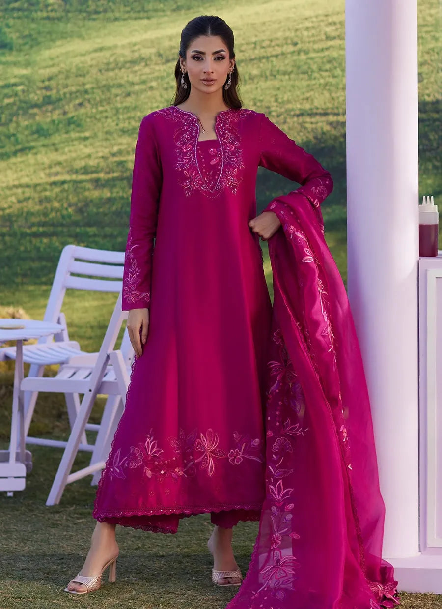 Woman in a pink embroidered outfit standing outdoors with greenery in the background