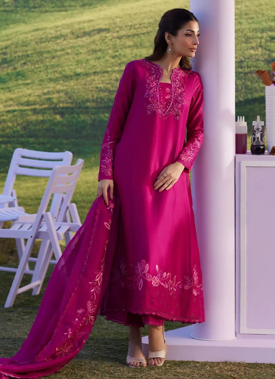 Woman in a pink embroidered outfit standing outdoors with white chairs and a green background