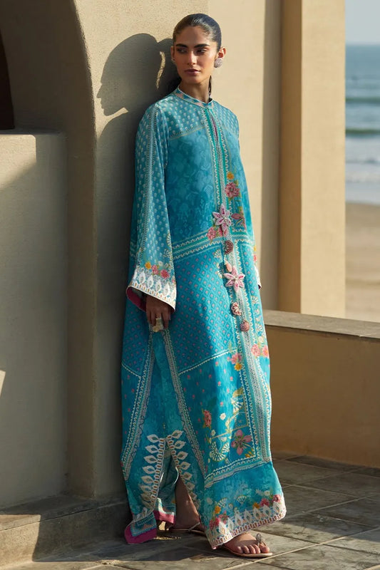 Woman wearing a blue embroidered traditional outfit by a window with a view of the ocean.