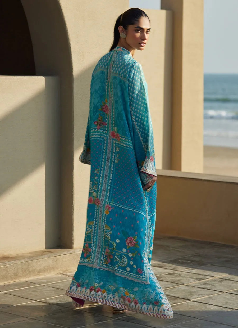 Woman wearing a blue embroidered shawl by a window with a view of water.