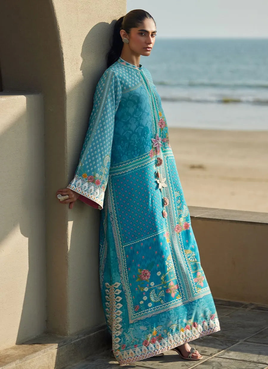 Woman in a blue embroidered dress standing by a beach.