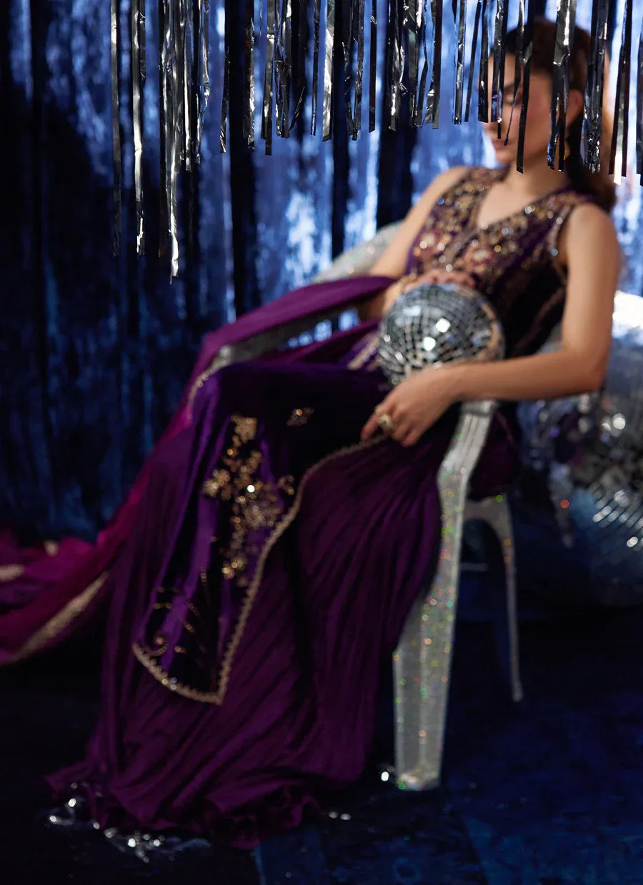 Woman in a purple evening gown with sequin details sitting on a chair against a dark background.