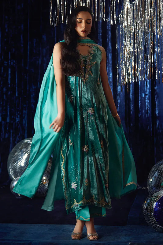 Woman in a teal traditional outfit with gold embroidery against a dark blue curtain background.