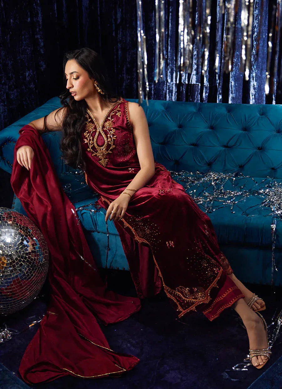 Woman in a red traditional outfit sitting on a blue couch with a disco ball and silver tinsel in the background.