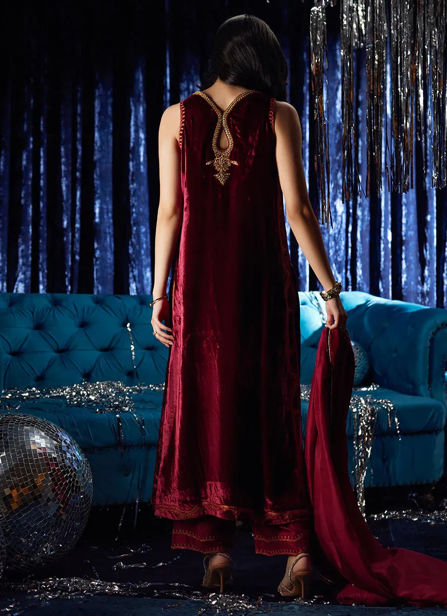Woman in a burgundy dress standing in a glamorous room with blue couch and decorative elements.