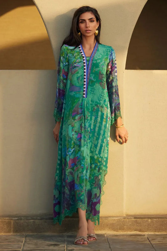 Woman wearing a green patterned dress standing against a beige wall.